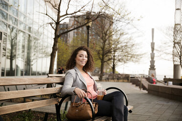 Porträt einer glücklichen Geschäftsfrau, die auf einer Bank am Fußweg sitzt - CAVF26265