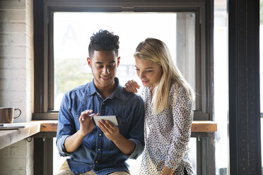 Lächelndes Paar, das ein Mobiltelefon benutzt, während es am Fenster eines Cafés sitzt - CAVF26277