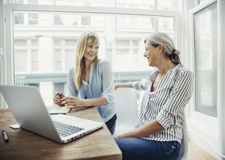 Happy businesswomen talking while sitting at desk in creative office - CAVF26284