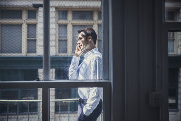 Seitenansicht eines Geschäftsmannes, der ein Smartphone benutzt, gesehen durch ein Fenster - CAVF26307