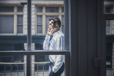 Side view of businessman using smart phone seen through window - CAVF26307