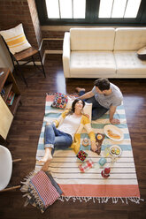 Hoher Blickwinkel auf ein Paar, das sich beim Essen auf einem Teppich entspannt - CAVF26316