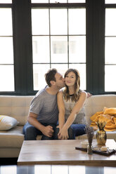 Mann küsst glückliche Freundin, während er zu Hause auf dem Sofa sitzt - CAVF26320