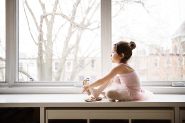 Mädchen sitzt auf einem Tisch und trägt Ballettschuhe vor einem Fenster - CAVF26346