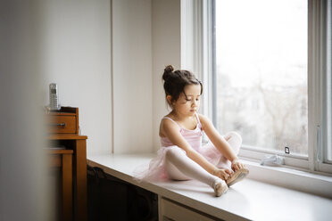 Mädchen mit Ballettschuhen, das zu Hause auf einem Tisch am Fenster sitzt - CAVF26347