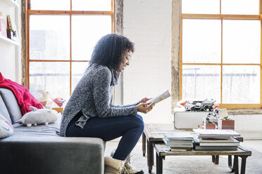 Side view of smiling businesswoman reading document while sitting in office - CAVF26358