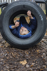 Porträt eines Jungen, der in einem Reifen auf einem Feld liegt - CAVF26374