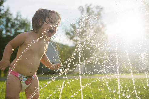 Verspieltes Mädchen bei den Sprinklern auf einem Feld im Hof stehend - CAVF26376