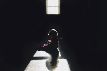 Side view of girl sitting in dark room - CAVF26382