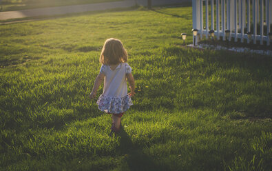 Rear view of girl walking on grassy field at yard during sunset - CAVF26389