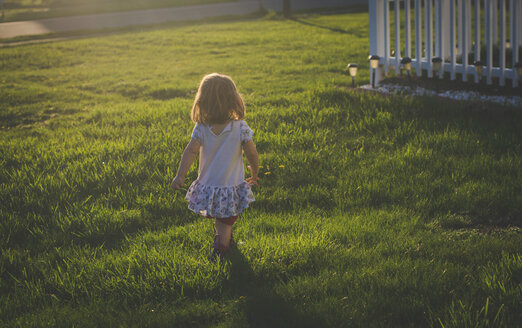 Rückansicht eines Mädchens, das während des Sonnenuntergangs auf einem grasbewachsenen Feld im Hof läuft - CAVF26389