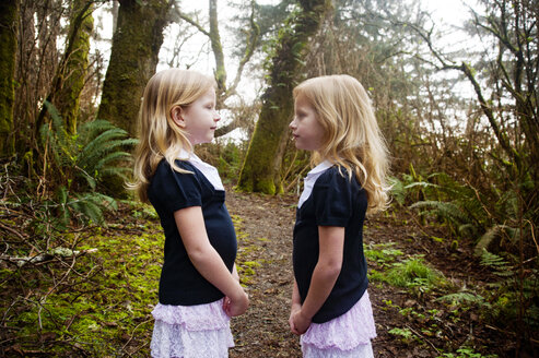 Twin girls standing on field against trees - CAVF26397