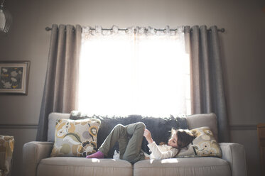 Girl using tablet computer while lying on sofa at home - CAVF26410