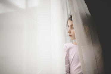 Mädchen mit geschlossenen Augen, das zu Hause am Fenstervorhang steht - CAVF26411