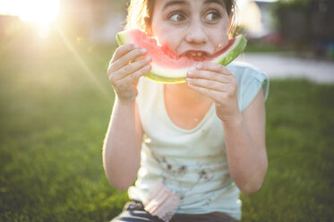 Girl eating watermelon while sitting on grassy field - CAVF26417
