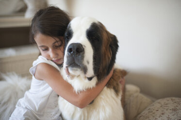 Girl embracing Saint Bernard while sitting on bed at home - CAVF26422