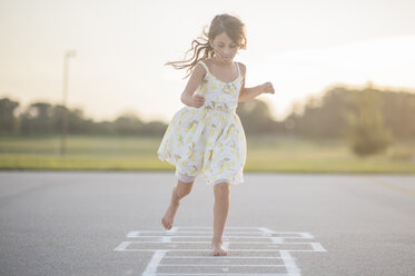 Full length of girl playing hopscotch on footpath against sky - CAVF26430