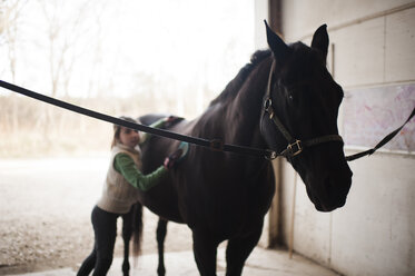 Girl standing by horse in stable - CAVF26431