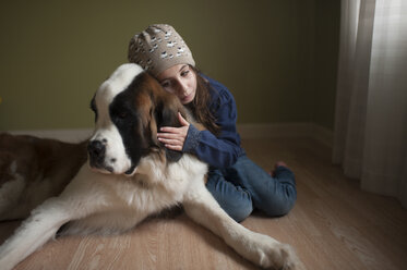 Mädchen umarmt Bernhardiner, während sie zu Hause auf dem Boden sitzt - CAVF26435