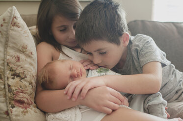 Siblings looking at baby boy while sitting on sofa - CAVF26447