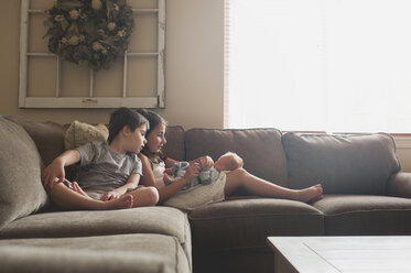 Geschwister spielen auf dem Sofa zu Hause mit dem kleinen Jungen - CAVF26449