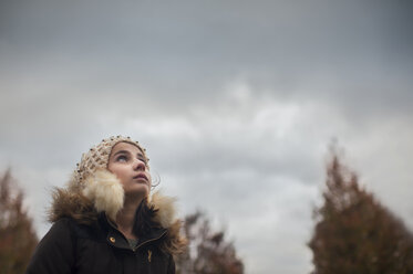 Thoughtful girl looking up while standing against cloudy sky - CAVF26456