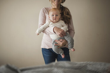 Mittelteil einer Mutter, die einen kleinen Jungen trägt, während sie zu Hause an der Wand steht - CAVF26460
