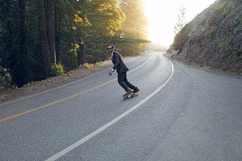 Geschäftsmann skateboarding auf der Straße an einem sonnigen Tag, lizenzfreies Stockfoto