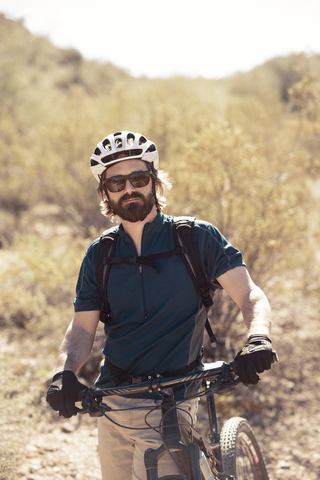 Porträt eines selbstbewussten Radfahrers, der mit seinem Fahrrad auf einem Berg steht, lizenzfreies Stockfoto