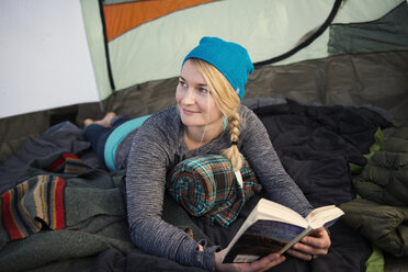 Lächelnde Frau mit Buch in der Hand im Zelt liegend - CAVF26634