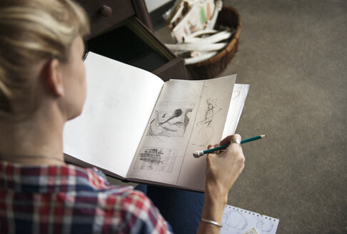 Künstlerin betrachtet Skizzen in einem Buch, während sie zu Hause sitzt - CAVF26656
