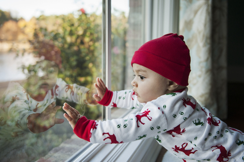 Kleiner Junge schaut durch ein Glasfenster zu Hause, lizenzfreies Stockfoto