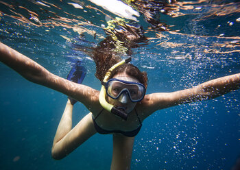 Portrait of young woman wearing goggles snorkeling undersea - CAVF26689