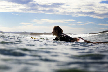 Side view of female surfer lying on surfboard in sea - CAVF26697