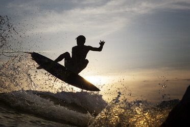 Junger männlicher Surfer, der bei Sonnenuntergang über das Meer springt - CAVF26700