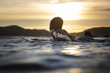 Junge auf Surfbrett im Meer liegend bei Sonnenuntergang - CAVF26701