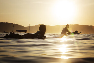 Female surfer lying on surfboard in sea during sunset - CAVF26703