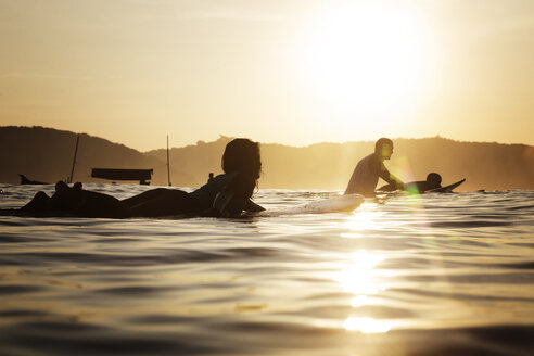 Weibliche Surferin auf dem Surfbrett im Meer liegend bei Sonnenuntergang - CAVF26703