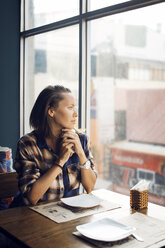 Nachdenkliche Frau schaut durch das Fenster, während sie in einem Café sitzt - CAVF26712