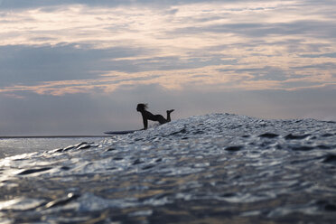 Seitenansicht einer Frau, die bei Sonnenuntergang auf dem Meer surft - CAVF26717