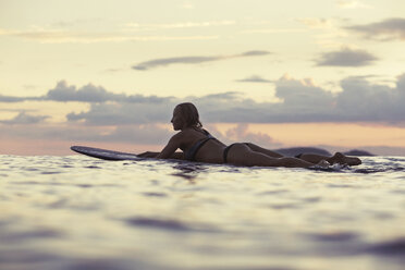 Side view of sensuous woman lying on surfboard in sea against sky during sunset - CAVF26722