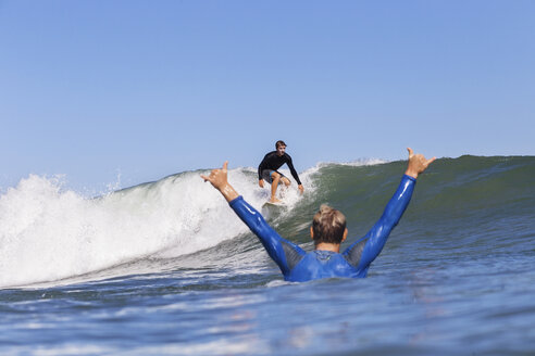 Mann jubelt, während er seinen Freund beim Surfen auf dem Meer gegen den klaren blauen Himmel beobachtet - CAVF26728