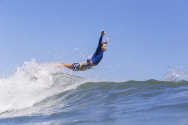 Side view of male surfer jumping on sea against clear blue sky - CAVF26729