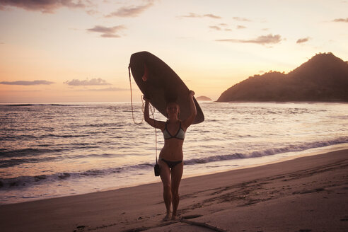 Porträt einer Surferin mit Surfbrett auf dem Kopf am Strand bei Sonnenuntergang - CAVF26731