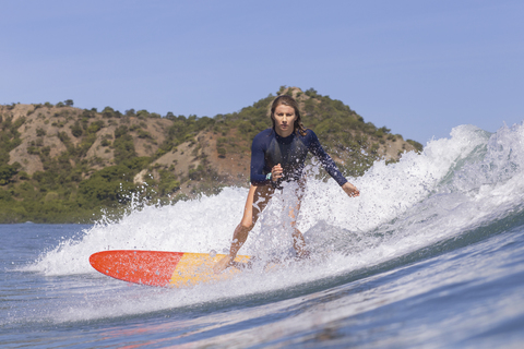 Selbstbewusste Frau beim Surfen auf dem Meer gegen den klaren blauen Himmel, lizenzfreies Stockfoto