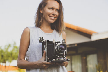 Mid adult woman holding old-fashioned video camera at yard - CAVF26738