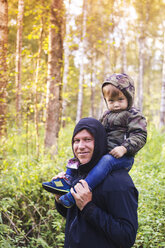 Porträt eines glücklichen Vaters, der seinen Sohn im Wald auf den Schultern trägt - CAVF26749