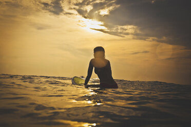 Frau sitzt auf einem Surfbrett im Meer gegen den Himmel - CAVF26768