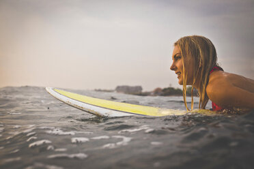 Woman looking away while lying on surfboard in sea against sky - CAVF26771