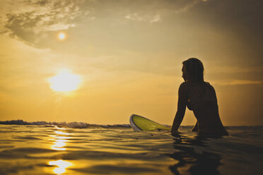 Frau sitzt auf einem Surfbrett im Meer bei Sonnenuntergang - CAVF26772